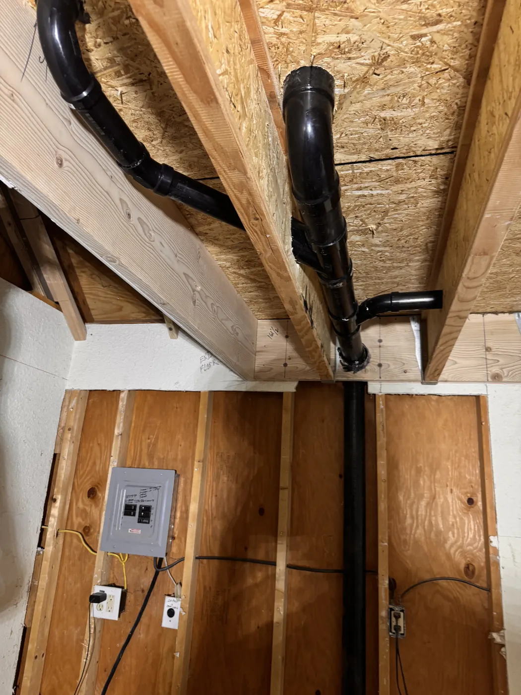 New black ABS drain and vent line routed through wood framing